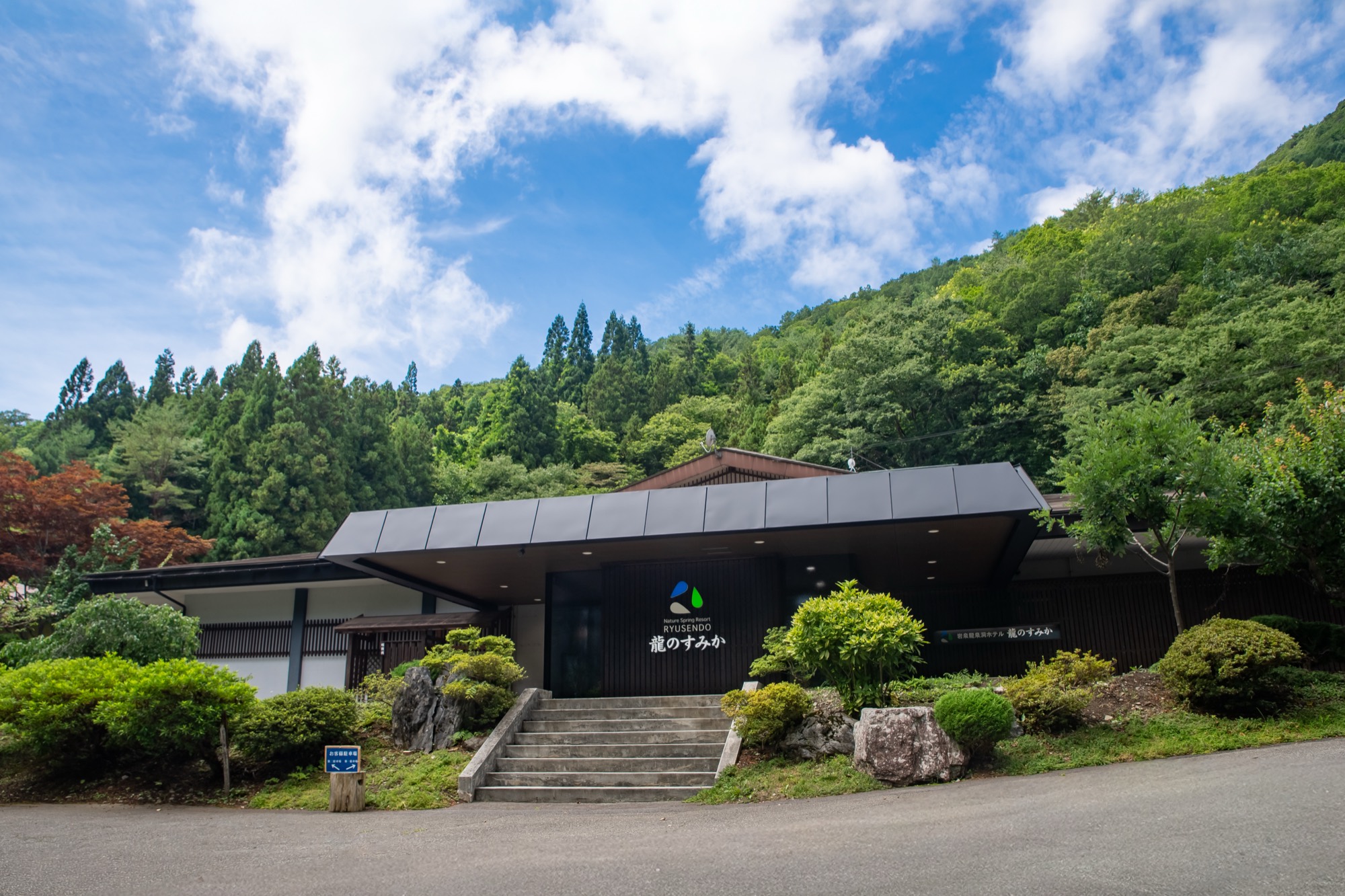 龍のすみか 外観。深い緑の山を背に、濃い焦茶の板張り